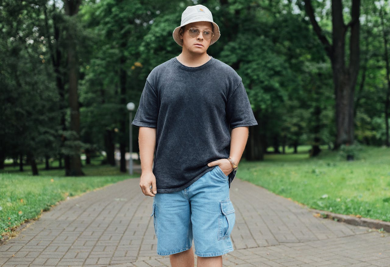 Young adult in summer attire enjoying a walk in a lush green park setting.